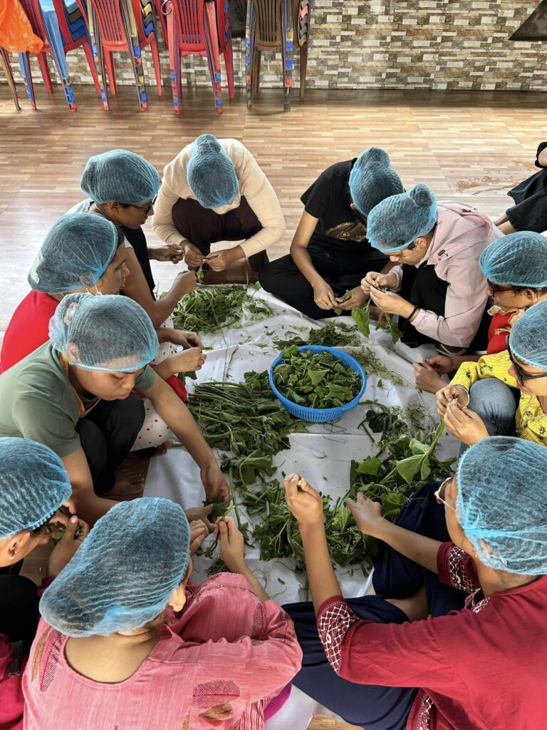 Participants learning and supporting each other to sort out green leafy veggies while Ms. Jimawati Lamkoliya instructs them