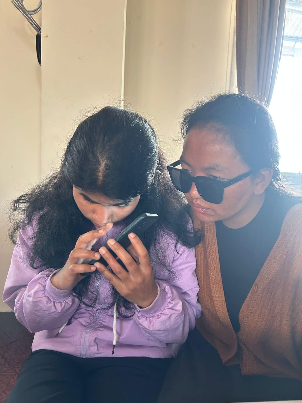 Two people sitting side by side, one holding a smartphone.